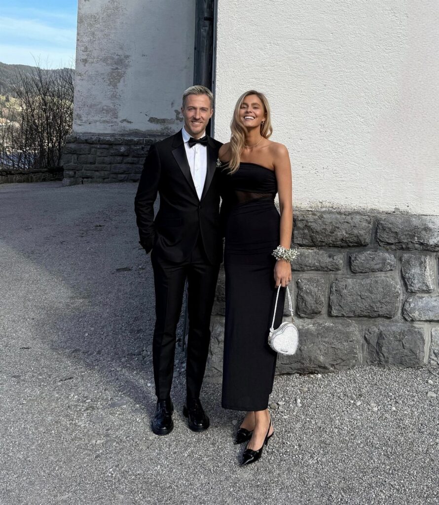 A man in a black tuxedo and a woman in a black evening gown smiling outdoors.