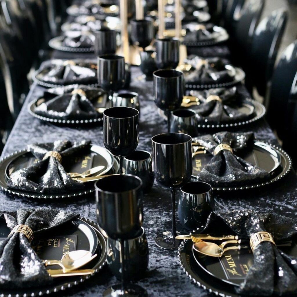 A formal dining table set with black sequined linens, black plates, and gold cutlery.