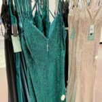 Emerald green and champagne shimmering prom dresses hanging on a retail clothing rack