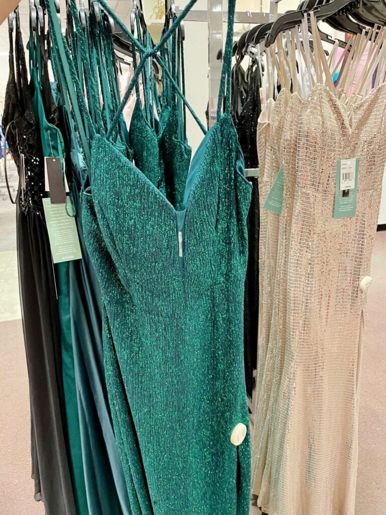 Emerald green and champagne shimmering prom dresses hanging on a retail clothing rack