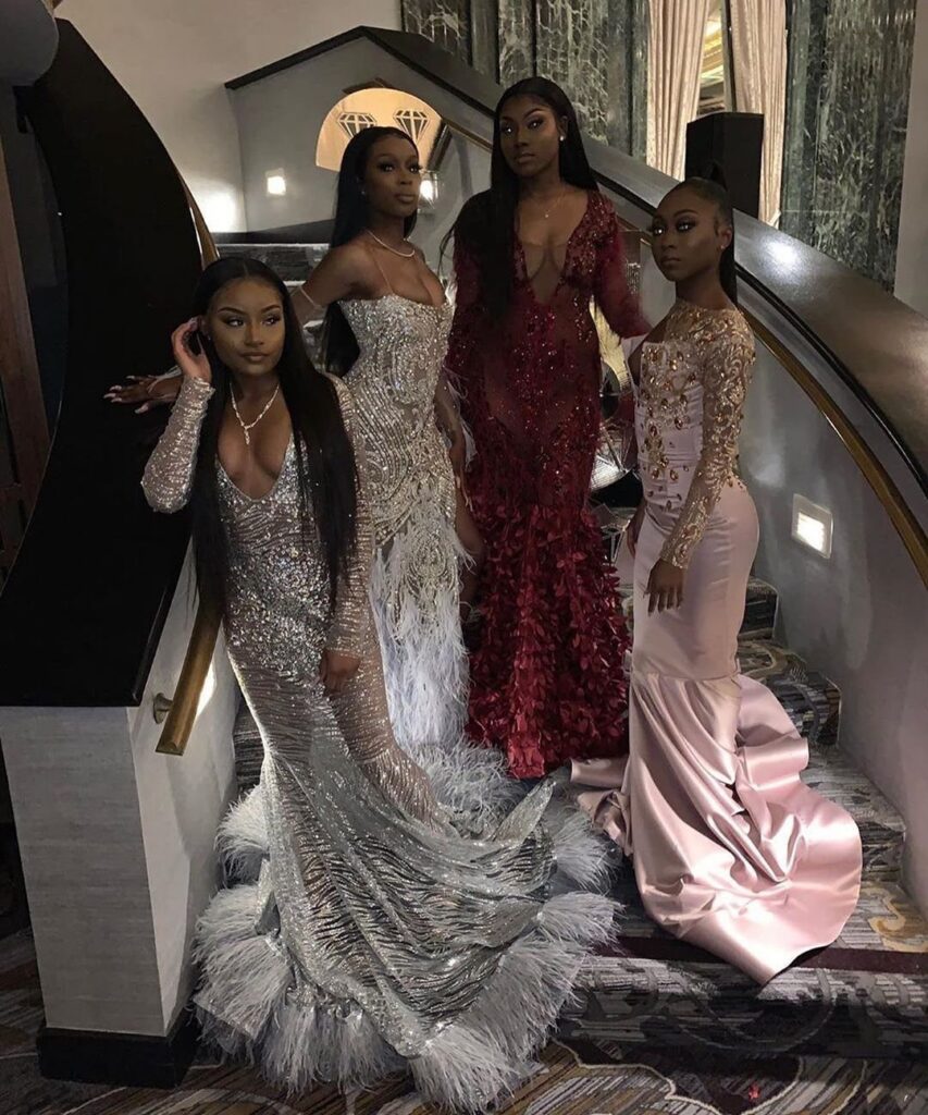Four women posing on a staircase wearing elegant, form-fitting mermaid-style evening gowns.