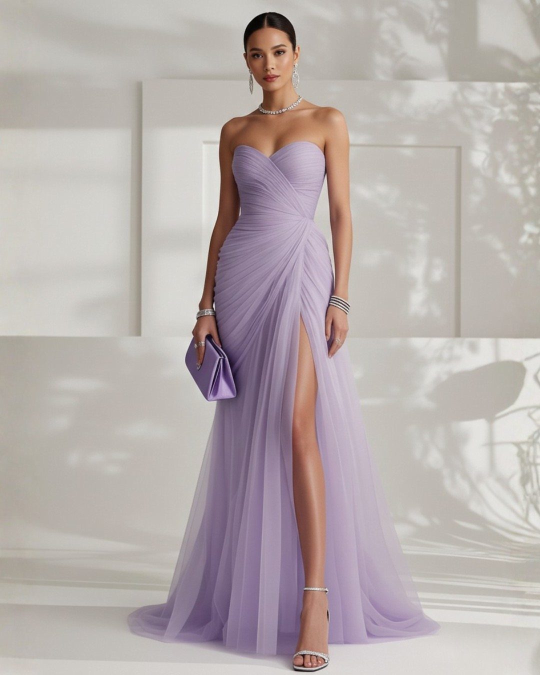 A woman in a lavender strapless formal gown with a high slit posing against a white wall.
