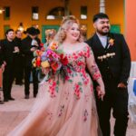 Woman in a champagne wedding dress with colorful floral embroidery holding a bouquet