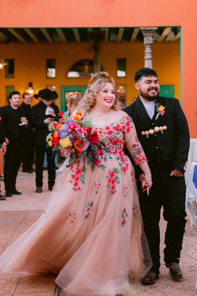 Woman in a champagne wedding dress with colorful floral embroidery holding a bouquet