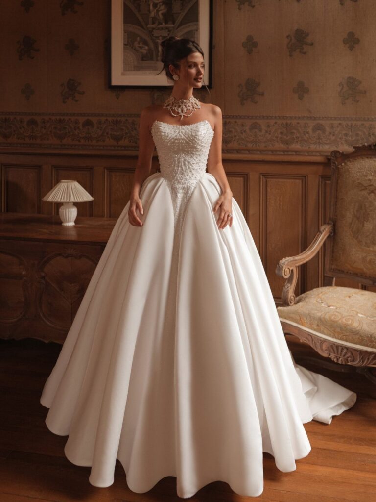 A woman in a white beaded strapless wedding dress standing in a classic wood-paneled room.